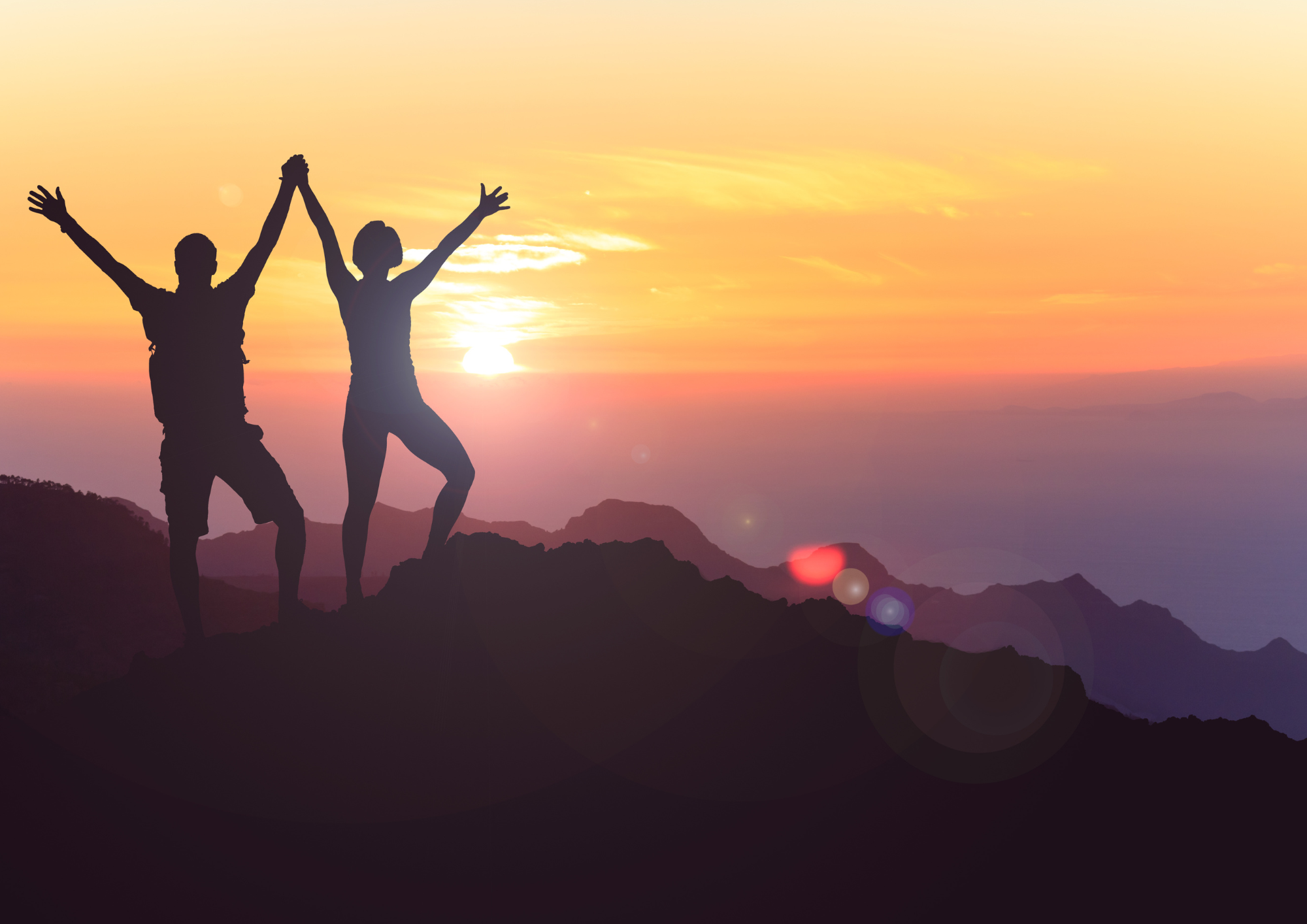 Photo of two people, arms raised in celebration with a sunset background