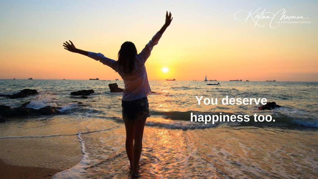 A photo of a woman paddling in the sea facing the sunrise, with her arms in the air to great the day, with the words "You deserve happiness too".